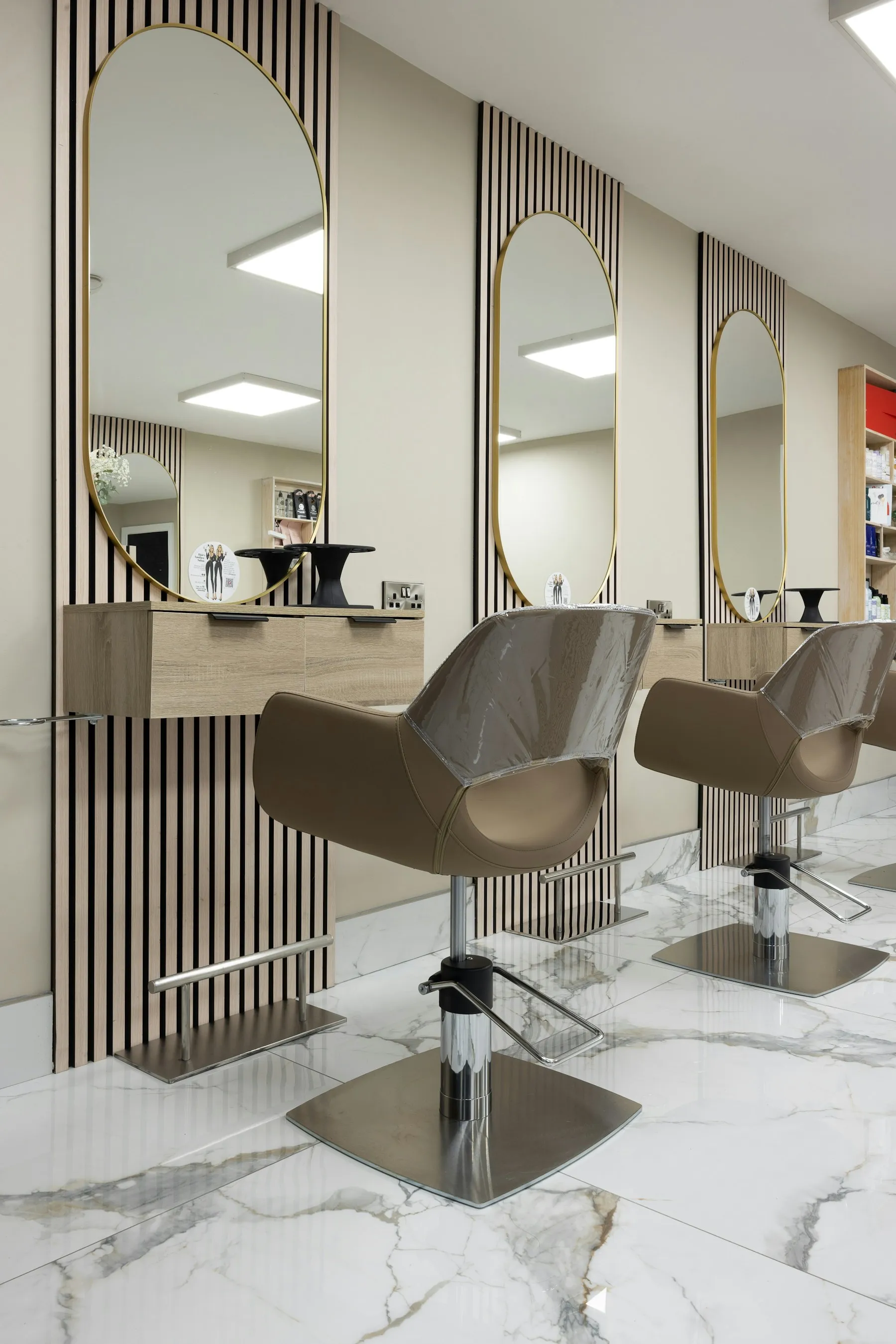 Two styling chairs facing oval mirrors in a bright salon with a marble floor