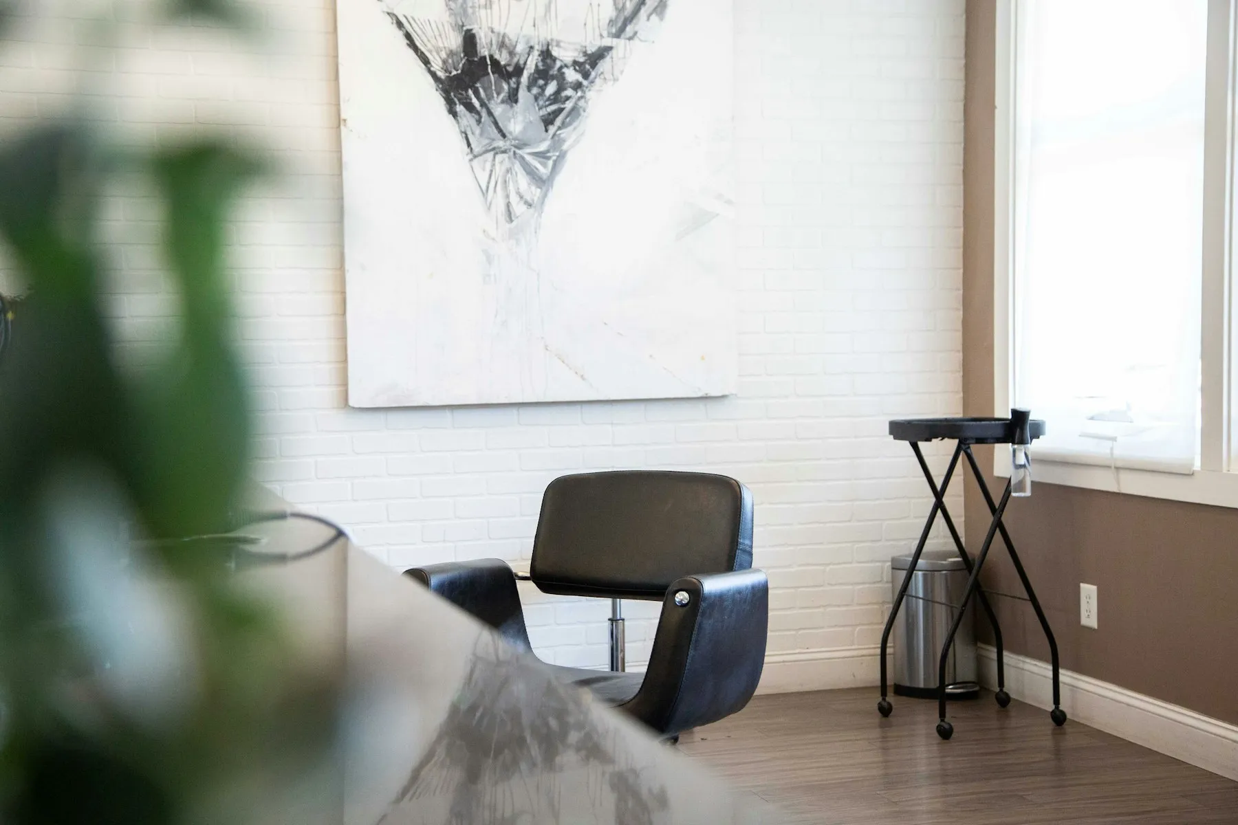An empty salon with a black styling chair, a white wall and a large framed print